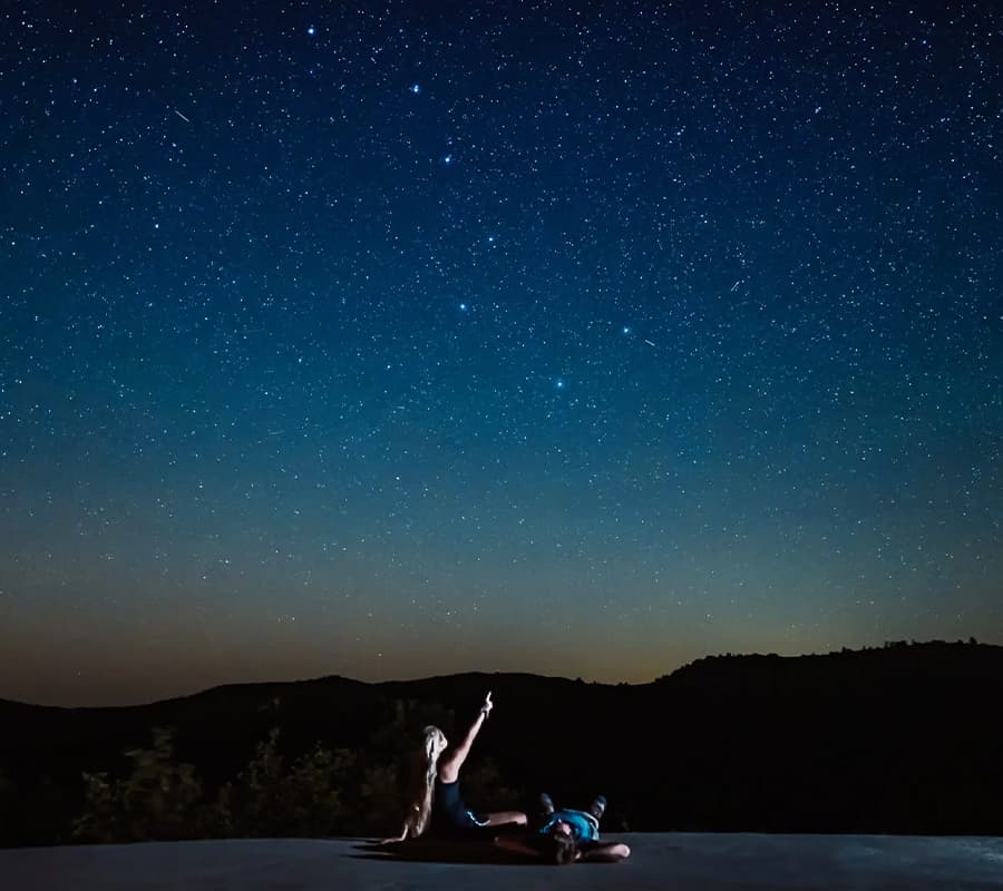 A person points to the starry night sky while another lies on the ground.