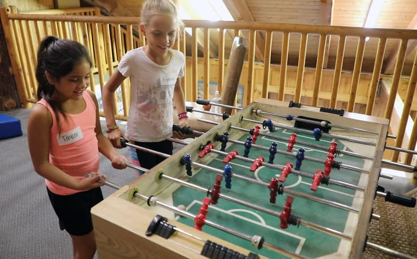Two girls play foosball in a wooden cabin setting.
