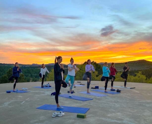 A group of women performing yoga poses on mats at sunset.