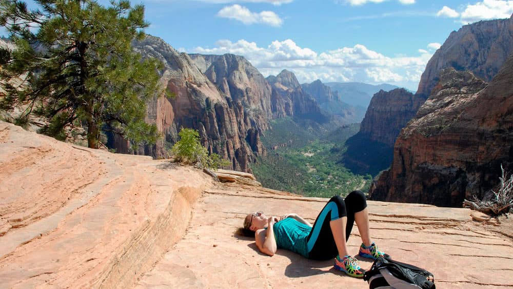A woman relaxes on a rocky ledge with a scenic mountain view.