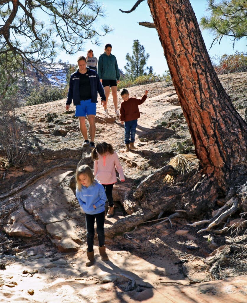 A group of children and adults hike along a rocky trail under a clear blue sky.