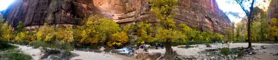 Panoramic view of a canyon with towering rock walls and vibrant yellow trees along a riverbank.