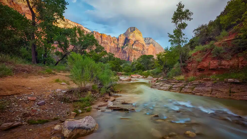 A serene river flows through a canyon landscape with vibrant cliffs and lush greenery.