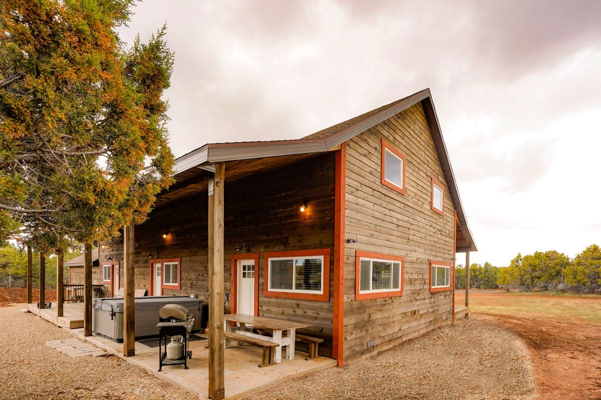 A modern wooden cabin with a covered porch and outdoor seating in a rural setting.