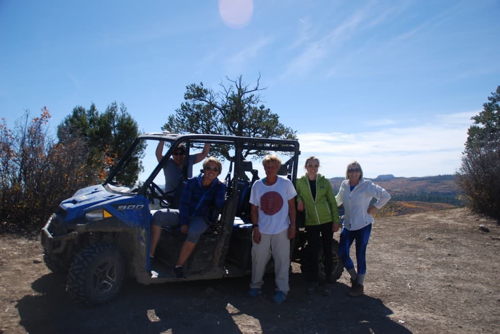 A group of five people poses by an off-road vehicle in a scenic outdoor setting.