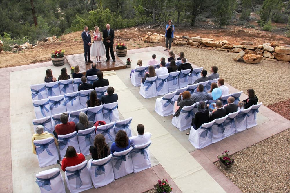 A wedding ceremony taking place outdoors with guests seated on chairs adorned with blue sashes.