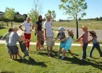 Children and adults in cowboy hats participate in a tug-of-war game on a grassy field.
