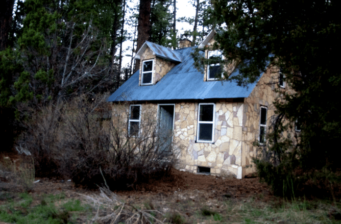 A small stone house surrounded by trees and overgrown vegetation.
