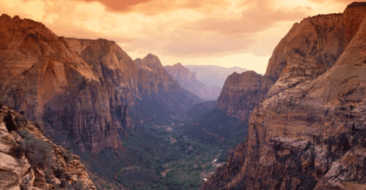 A sweeping view of a canyon at sunset, with towering rock formations and a valley below.