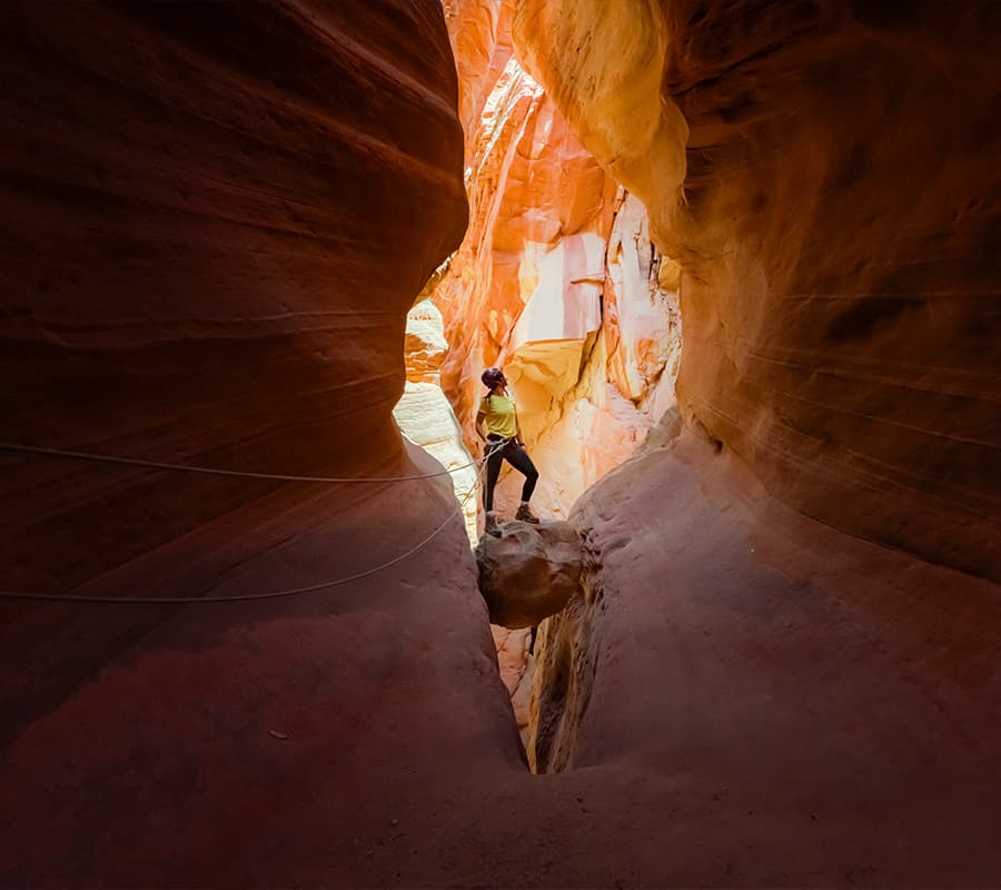 A climber navigates a narrow, colorful sandstone canyon.
