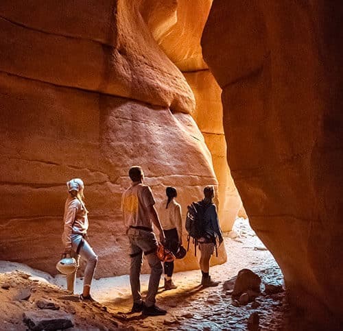Four hikers explore a narrow, sunlit canyon.