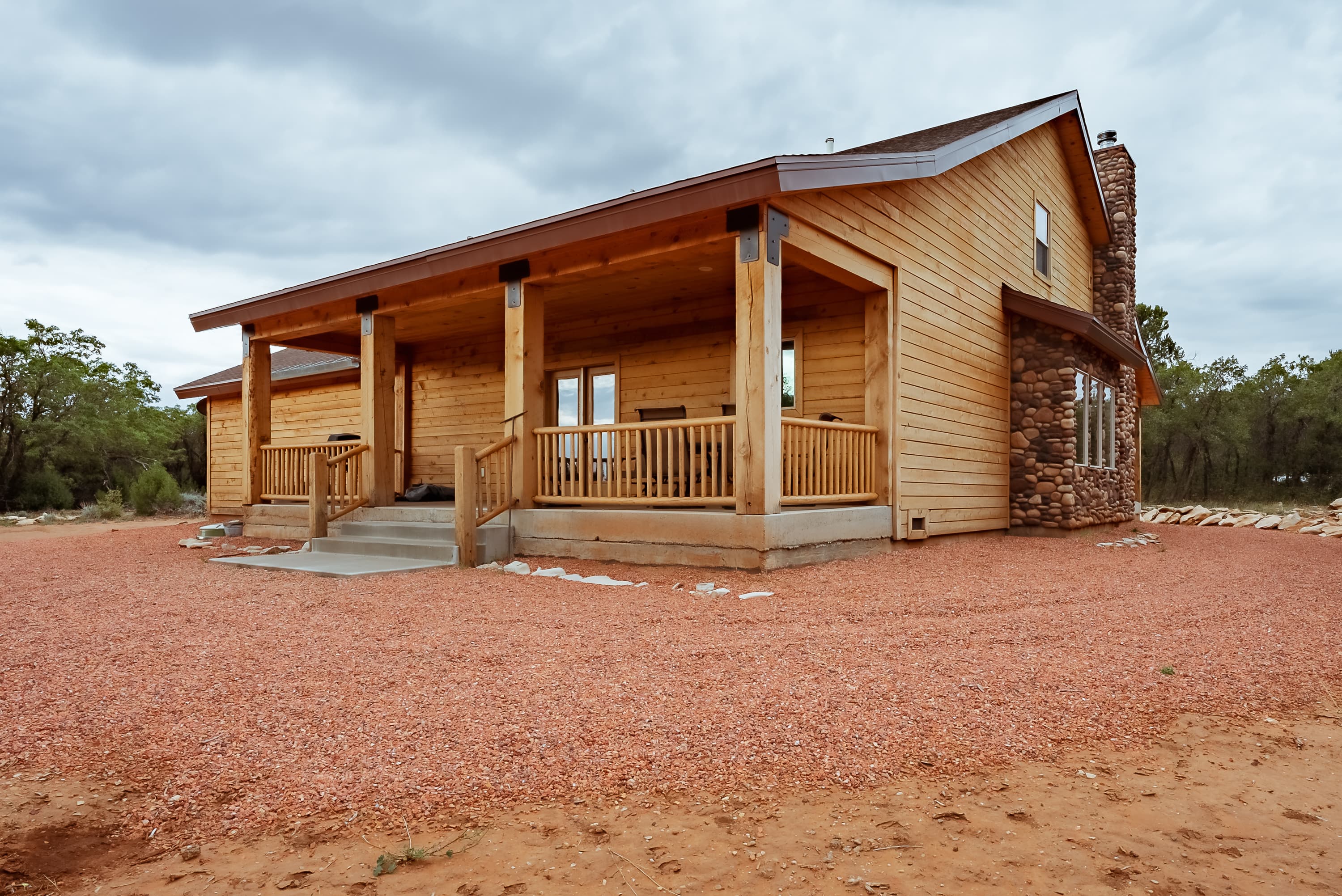 A modern log cabin with a stone facade and a front porch surrounded by gravel.