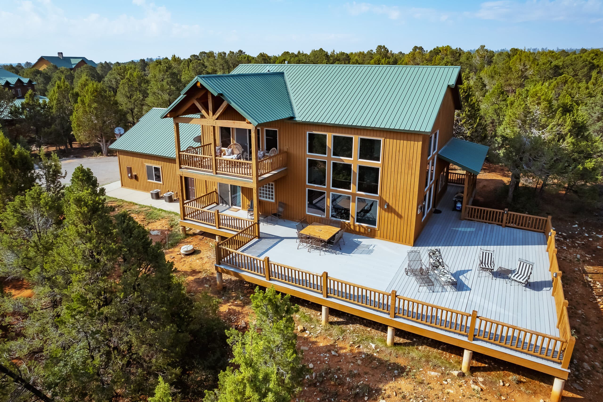 A spacious wooden house surrounded by trees, featuring large windows and a deck with seating.