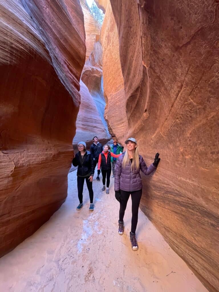 A group of people walks through a narrow, vibrant canyon with red rock walls.