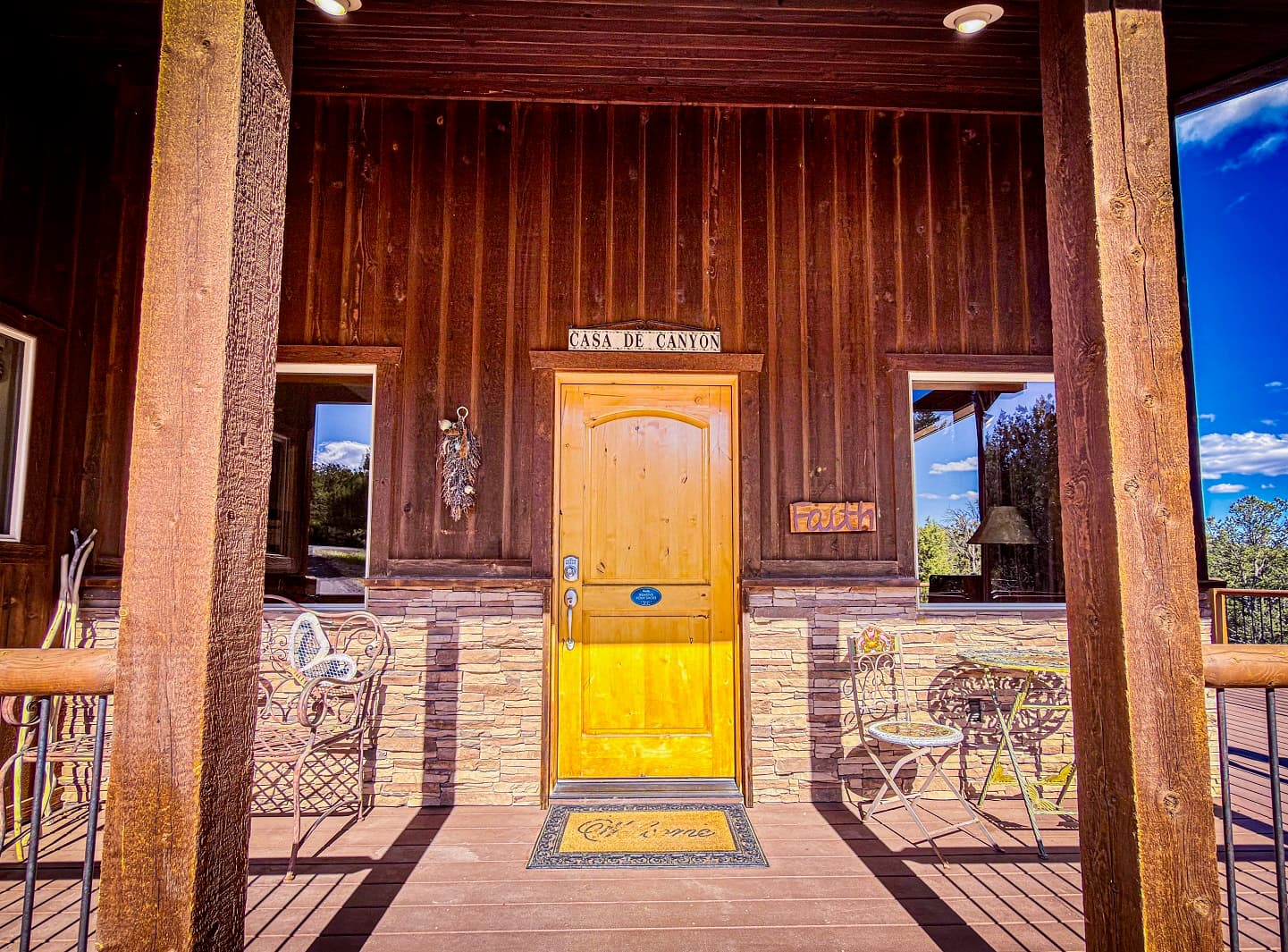 A wooden front door with a stone foundation, flanked by two windows and porch seating, labeled "Casa de Canyon."