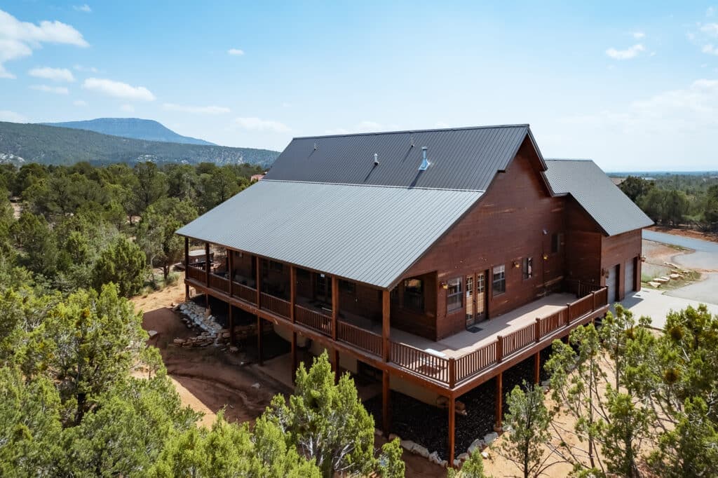 A large wooden house with a metal roof, surrounded by trees and scenic hills.