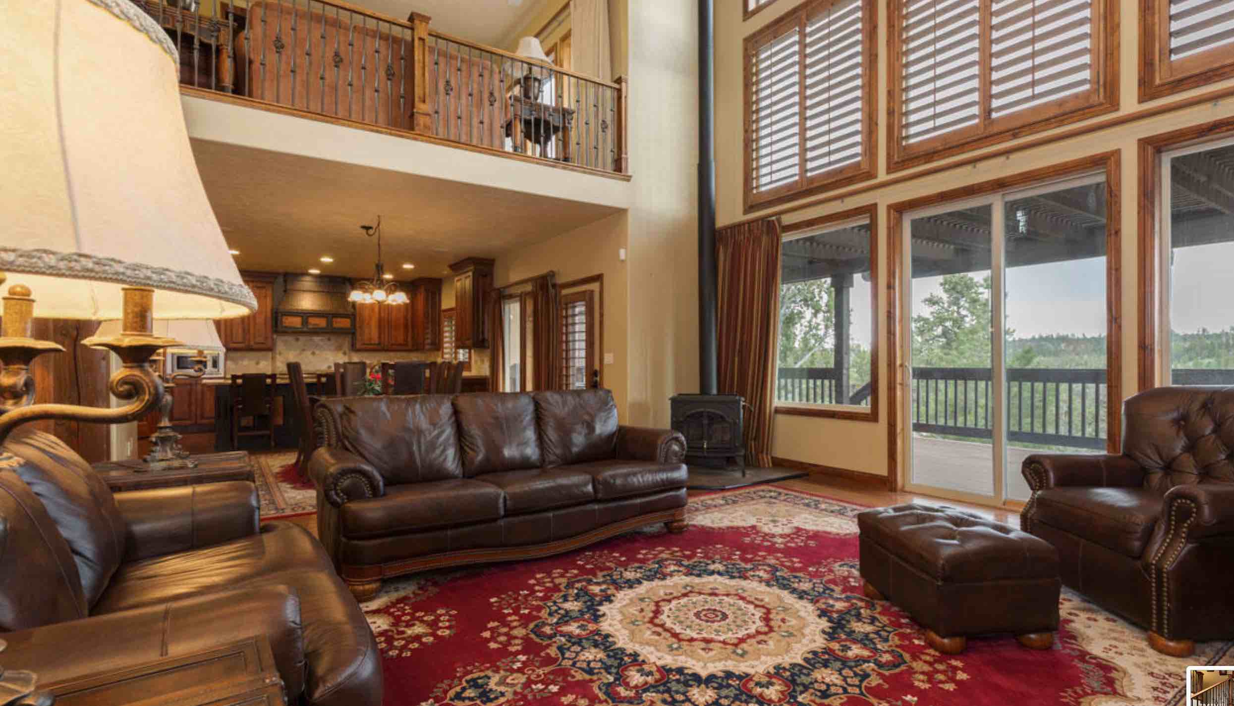 A spacious living room featuring leather sofas, a large area rug, and windows showcasing outdoor views.