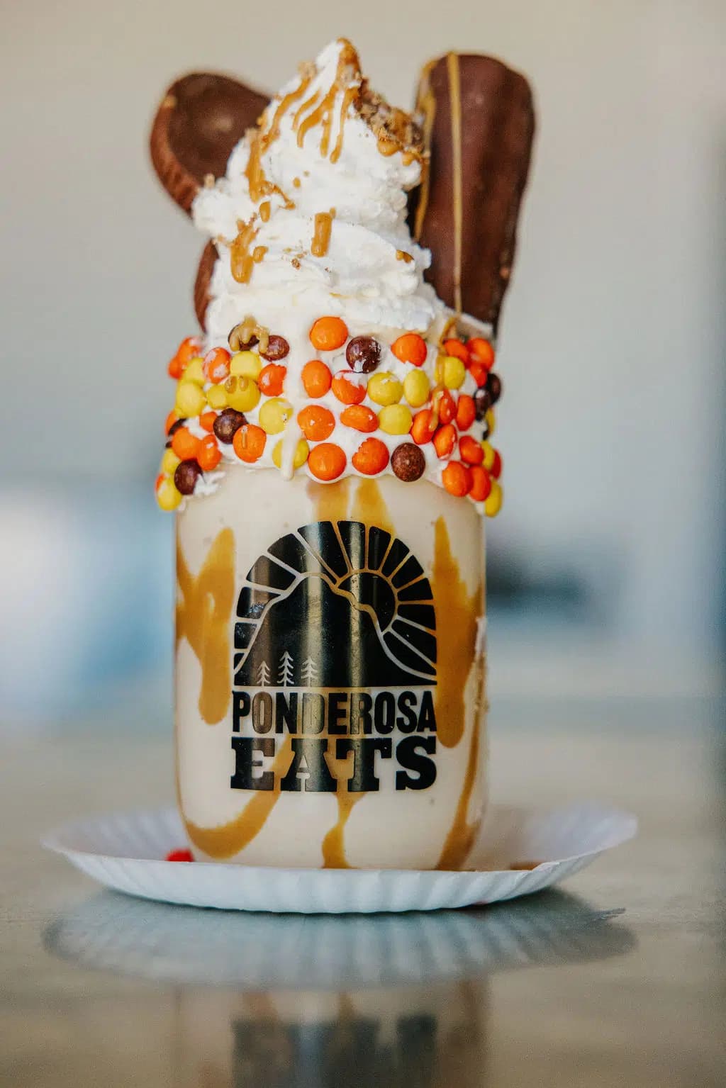 A decorated milkshake topped with whipped cream, caramel, and candy in a glass jar.
