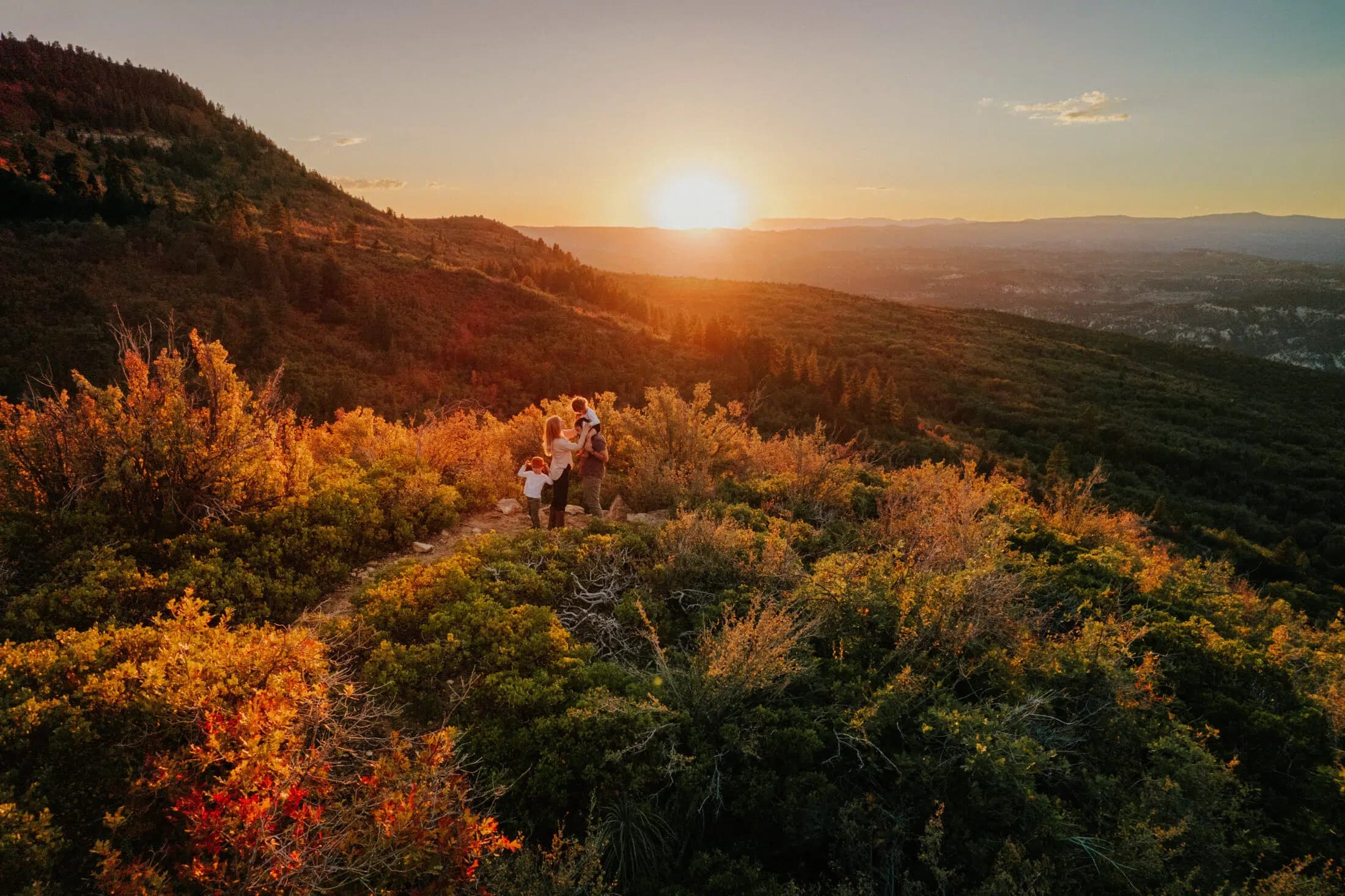 A group of friends stands on a hillside overlooking a vibrant sunset.