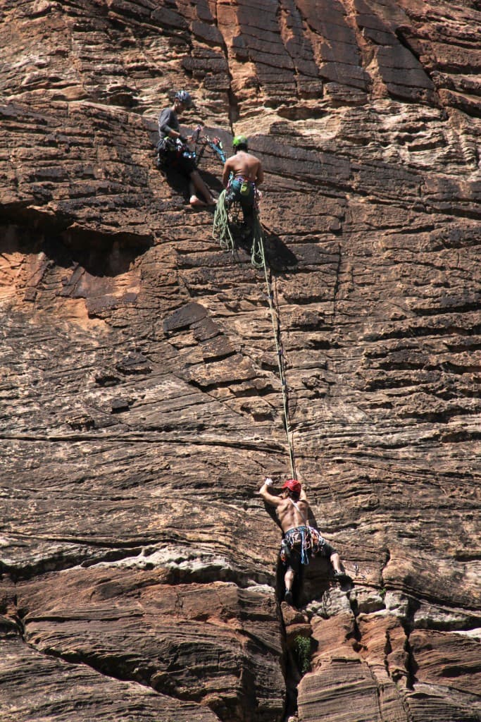 Two climbers ascend a rocky cliff while a third climber hangs below.