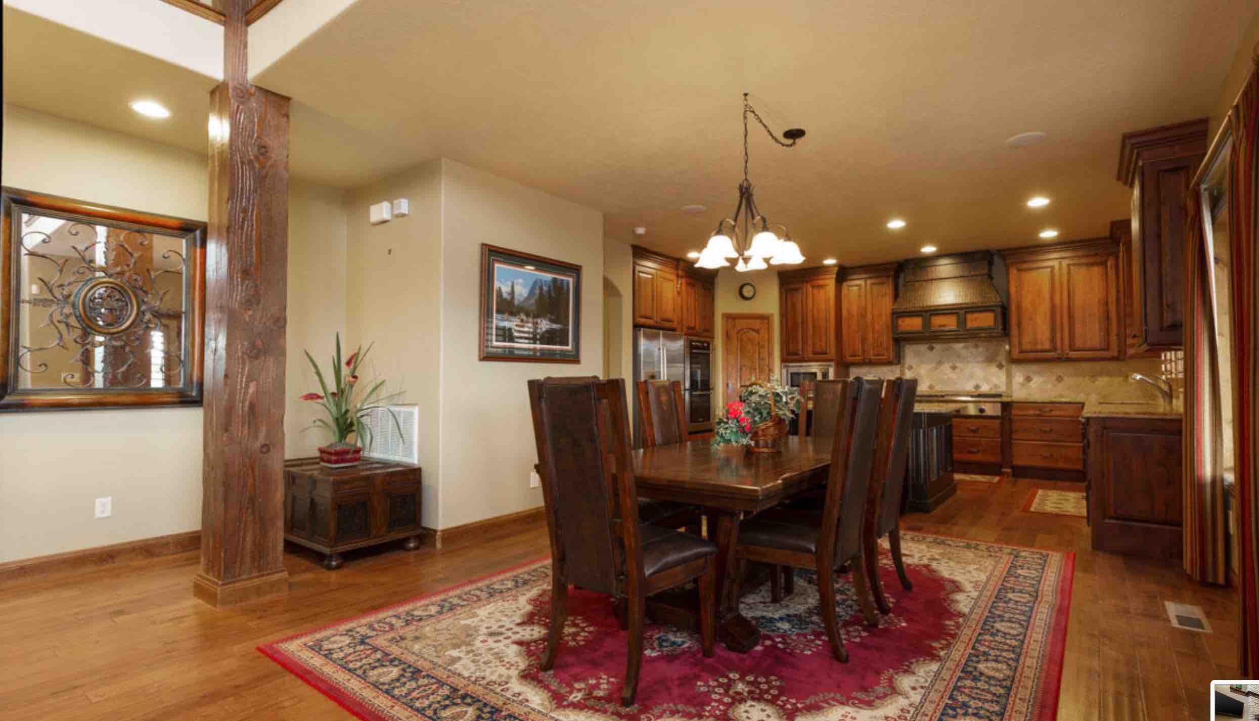 A warm, rustic dining area featuring a large wooden table, leather chairs, and a cozy kitchen in the background.