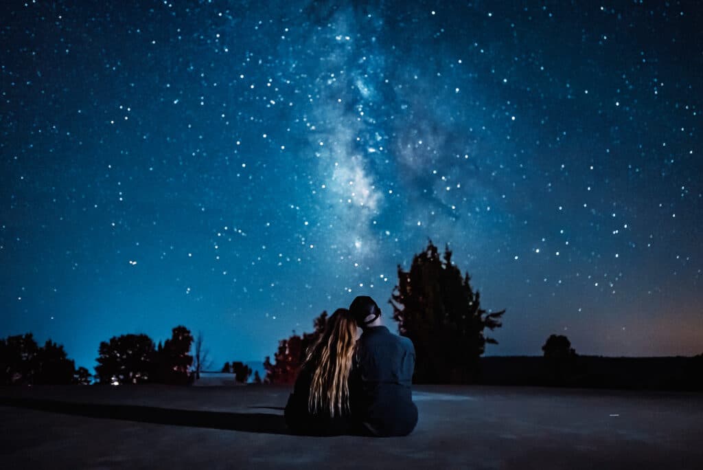 A couple sits closely together under a star-filled sky.