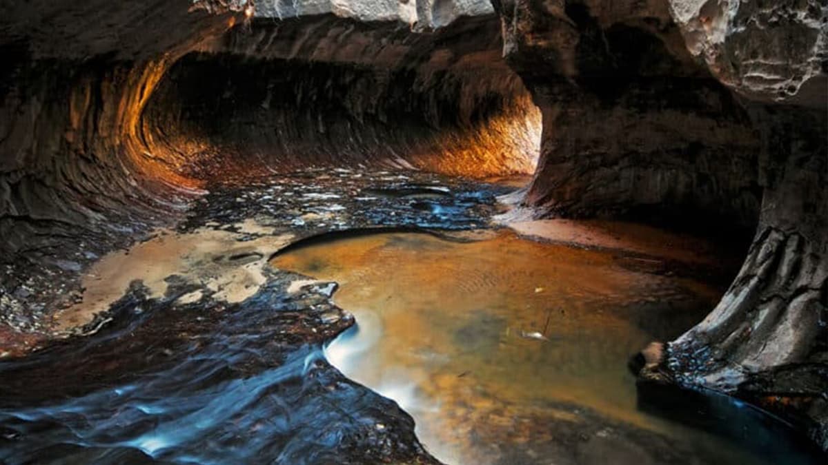 A narrow canyon with flowing water and illuminated rock formations.