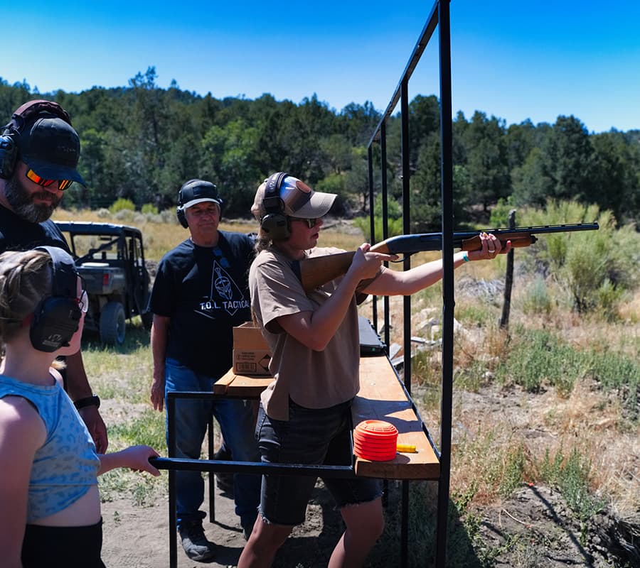 A person aims a firearm at a shooting range while being observed by others.