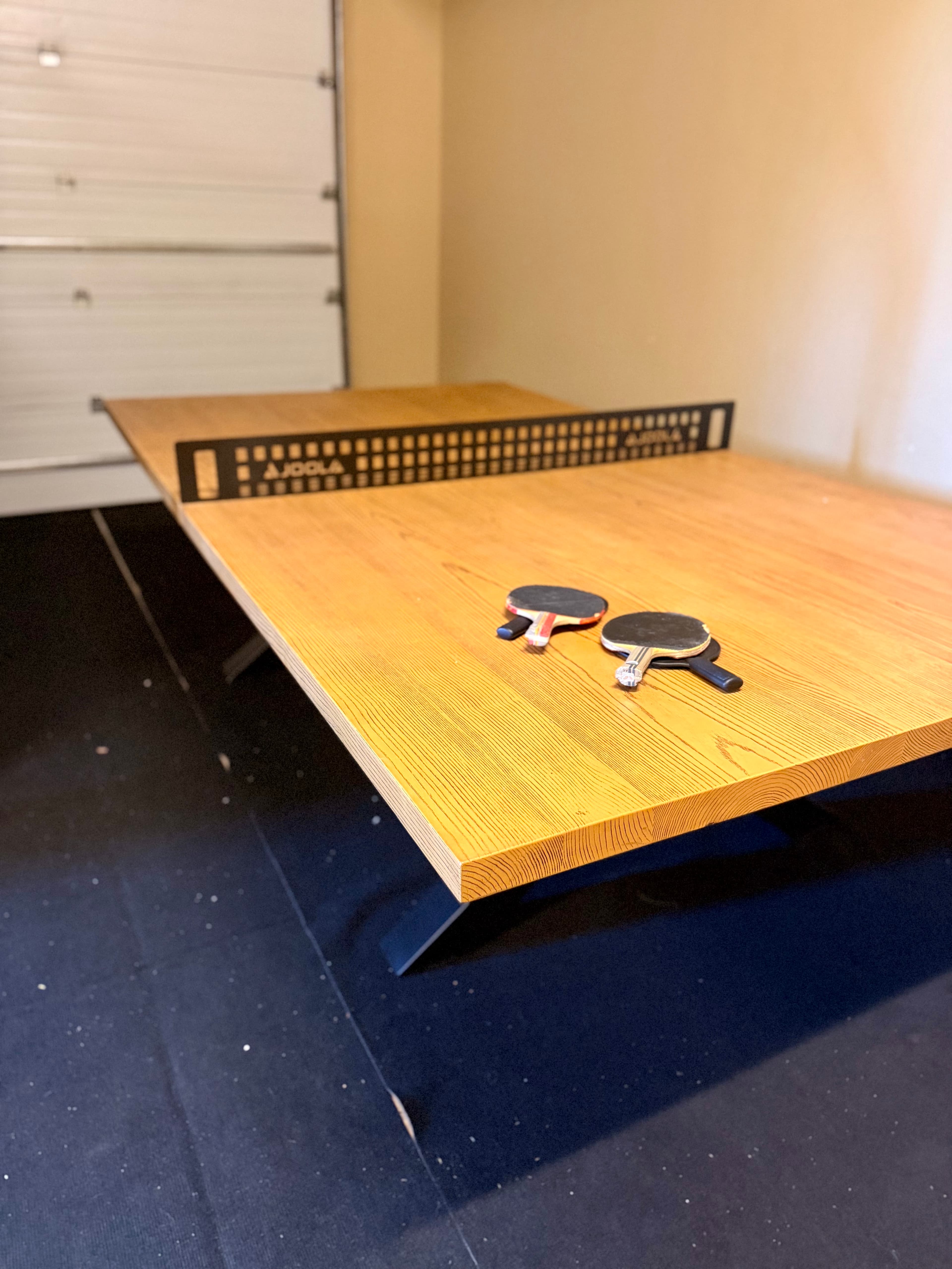 A wooden table set up for table tennis with paddles and a net.