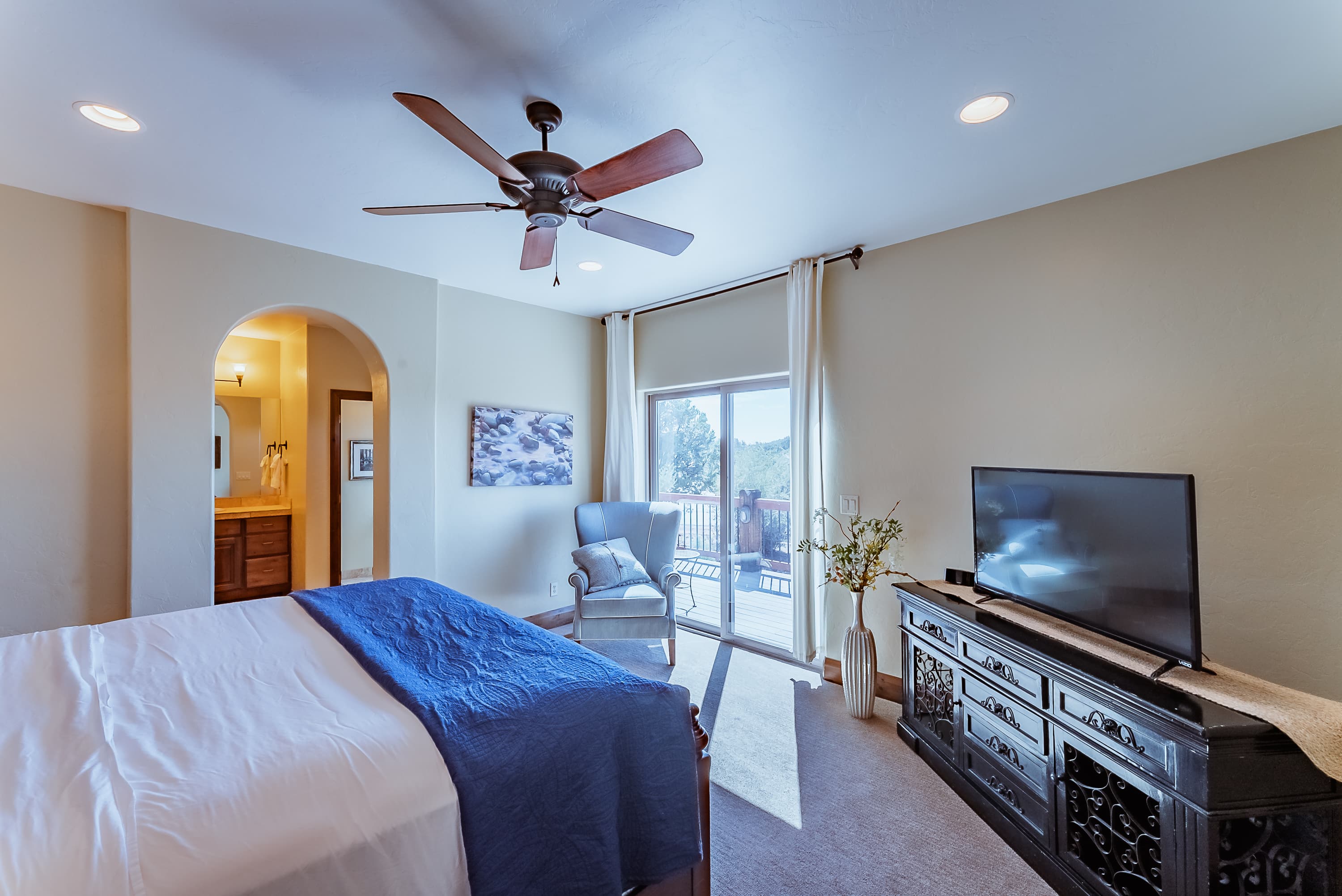 Cozy bedroom featuring a queen bed, ceiling fan, a TV, and access to a balcony with natural light.