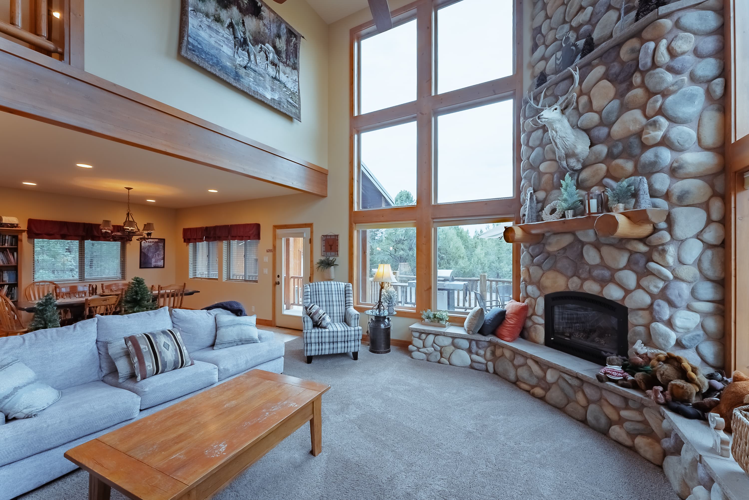 A cozy living room featuring a stone fireplace, large windows, and comfortable furniture.