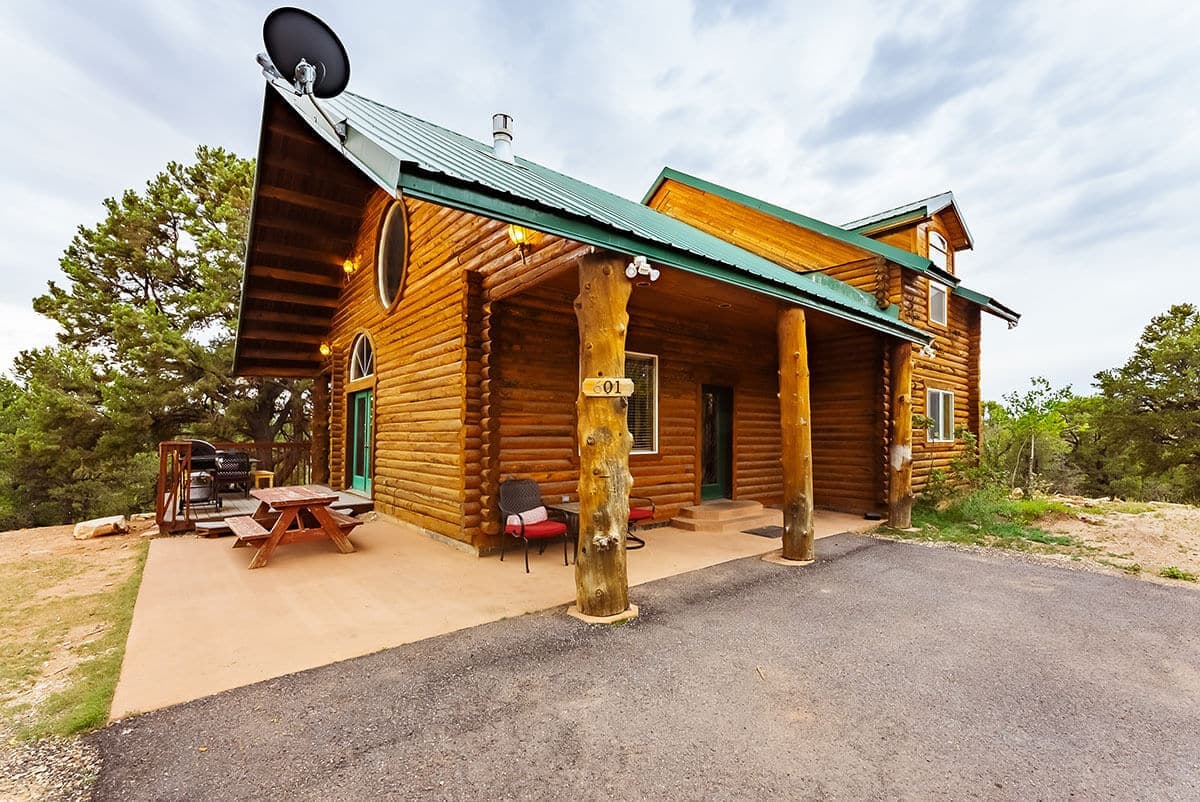 A rustic wooden cabin with a green roof, featuring a porch and surrounded by trees.