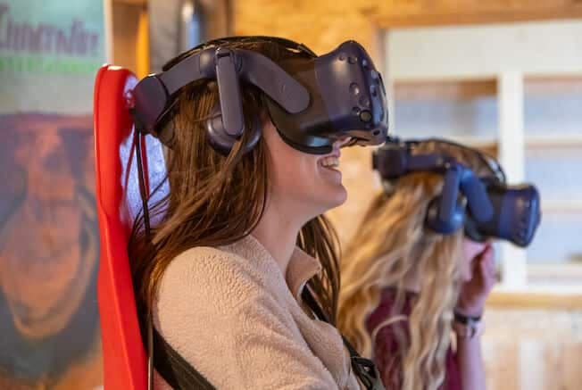 Two women smile while wearing virtual reality headsets in a cozy setting.