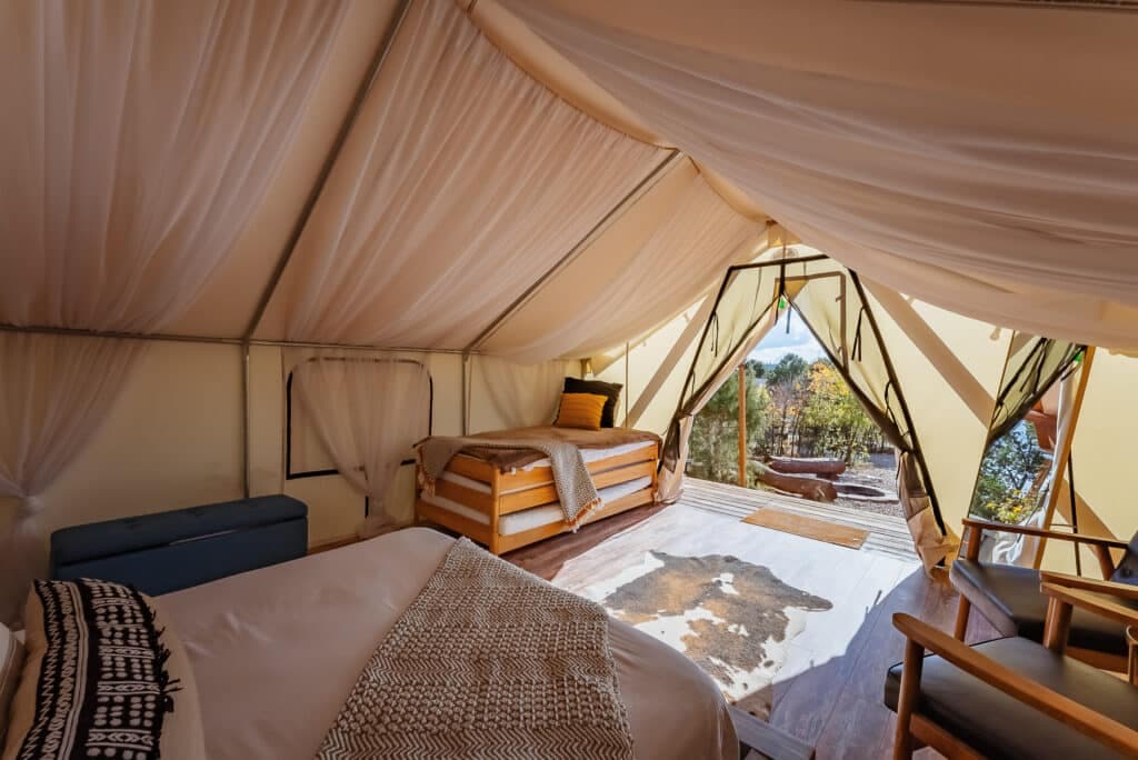 Interior of a spacious glamping tent featuring two beds, natural light, and a view of the outdoors.