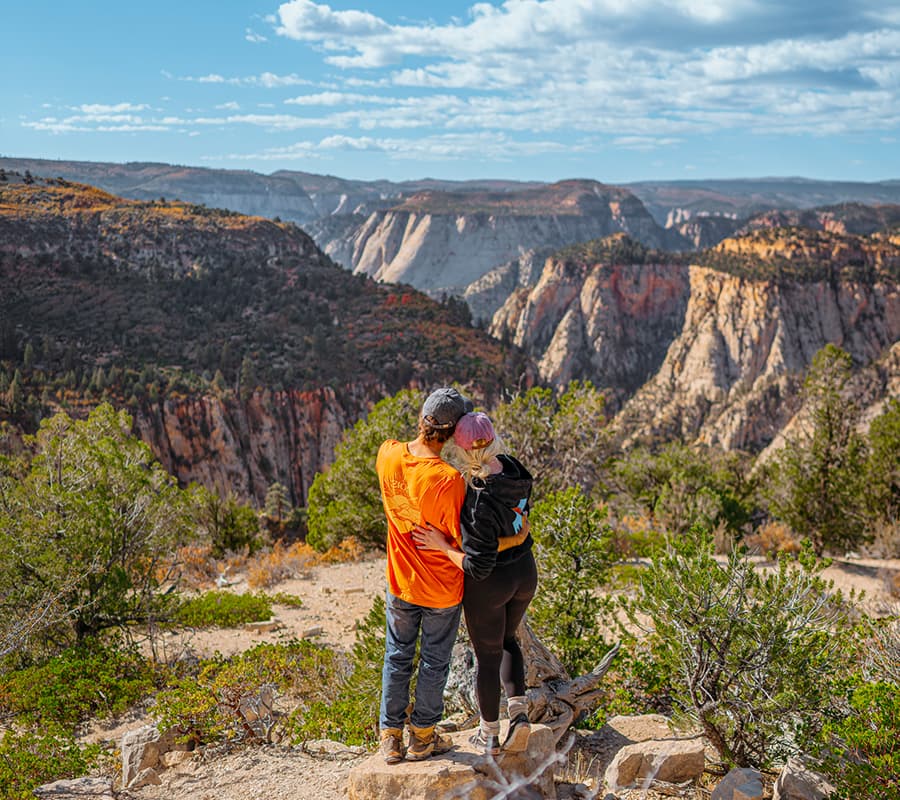A couple embraces while overlooking a scenic canyon landscape.