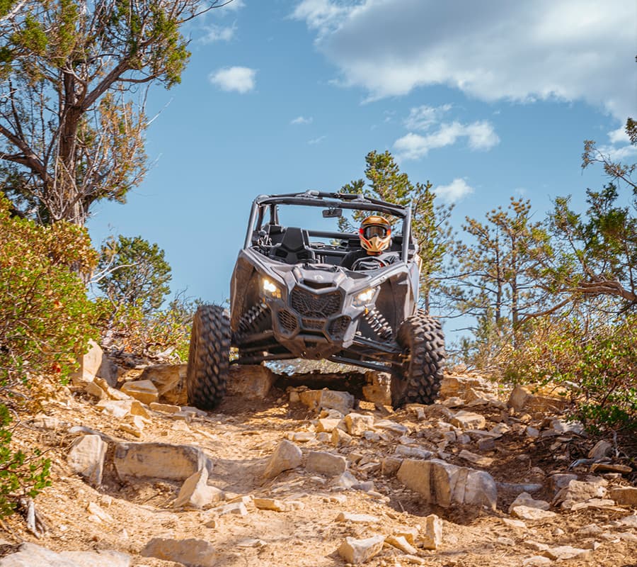 A rugged off-road vehicle navigates a rocky trail under a blue sky.