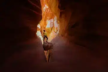 A person standing on a rock inside a narrow, vibrant orange canyon.