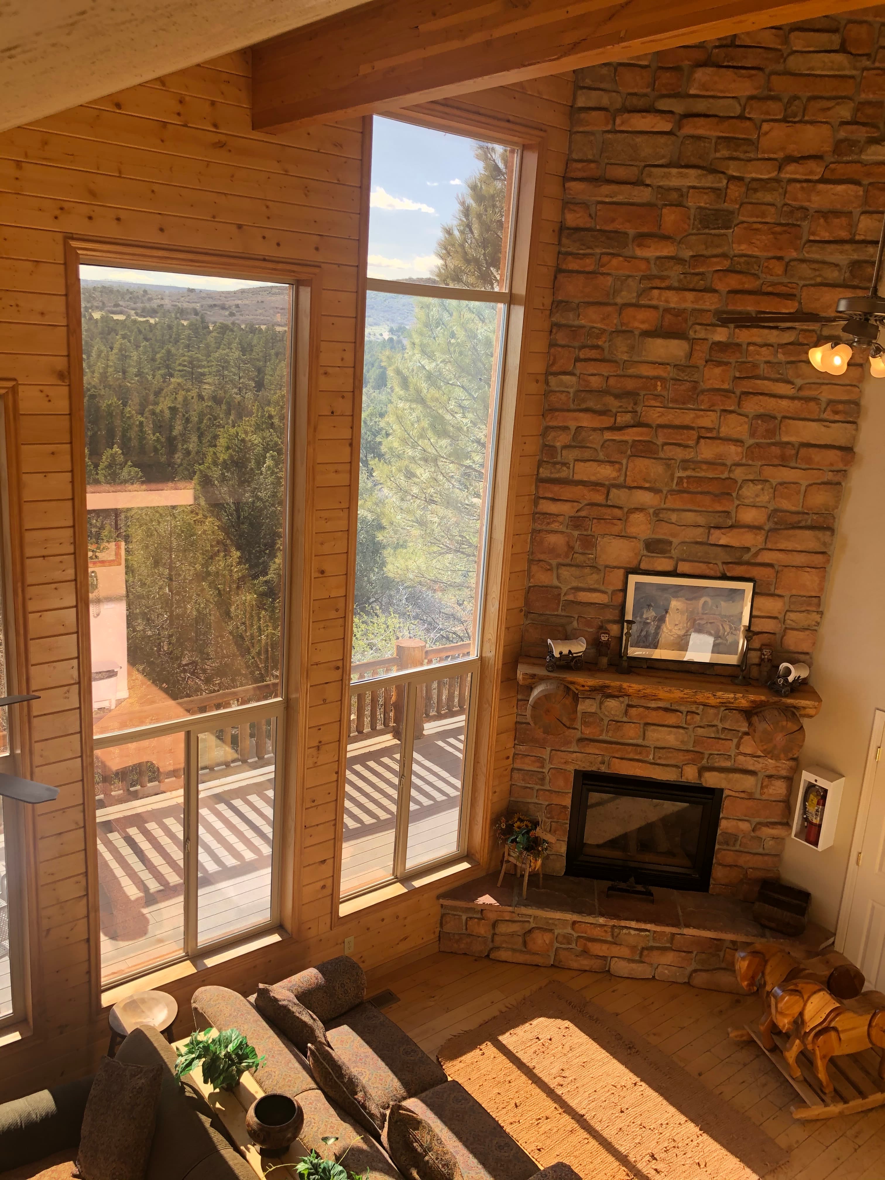 Bright living room with large windows and a stone fireplace, overlooking a forested landscape.