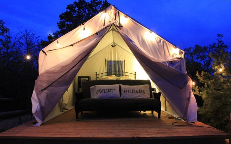 A tent with fairy lights and a bed inside, set against a twilight sky.
