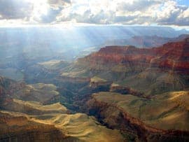 A sunlit view of the Grand Canyon with layered rock formations and clouds above.