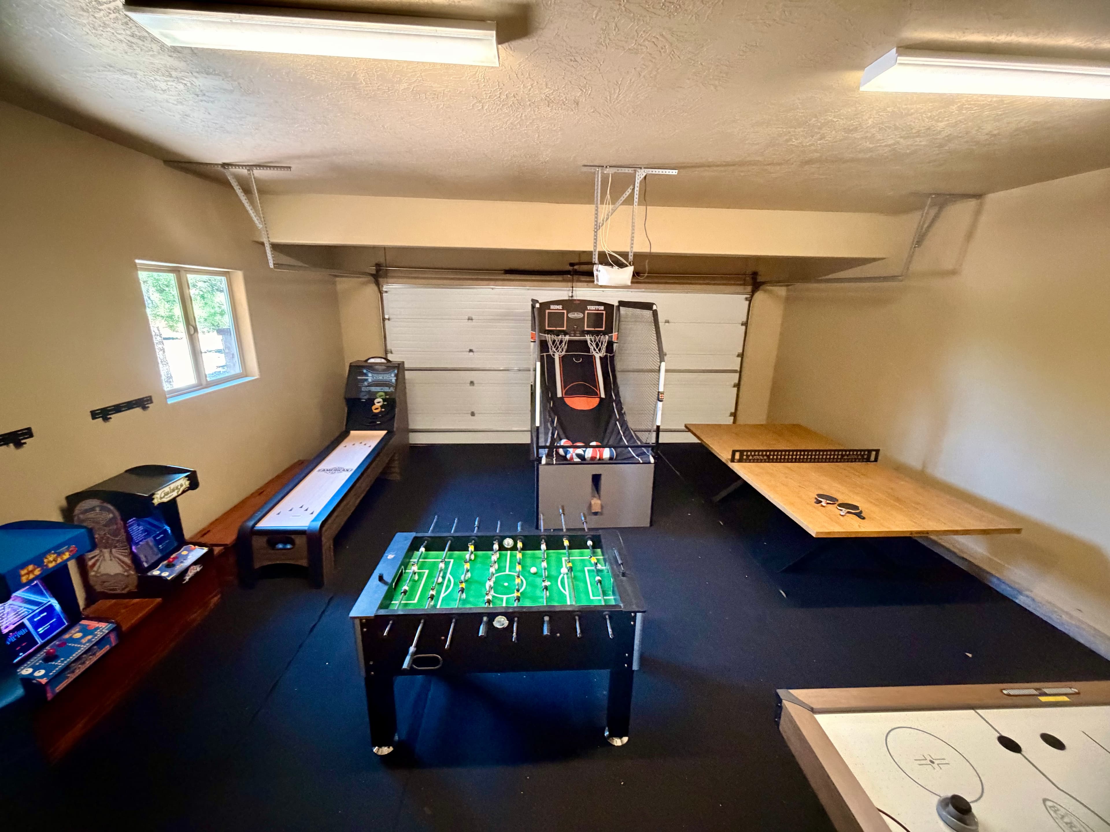 A game room featuring a foosball table, arcade machines, a basketball shooting game, and air hockey table.