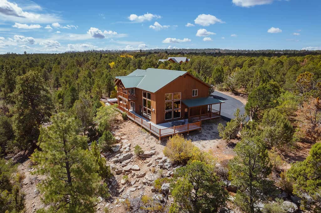 A spacious wooden house surrounded by lush greenery and trees under a partly cloudy sky.