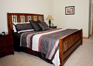 A cozy bedroom featuring a wooden bed with striped bedding and a bedside lamp.