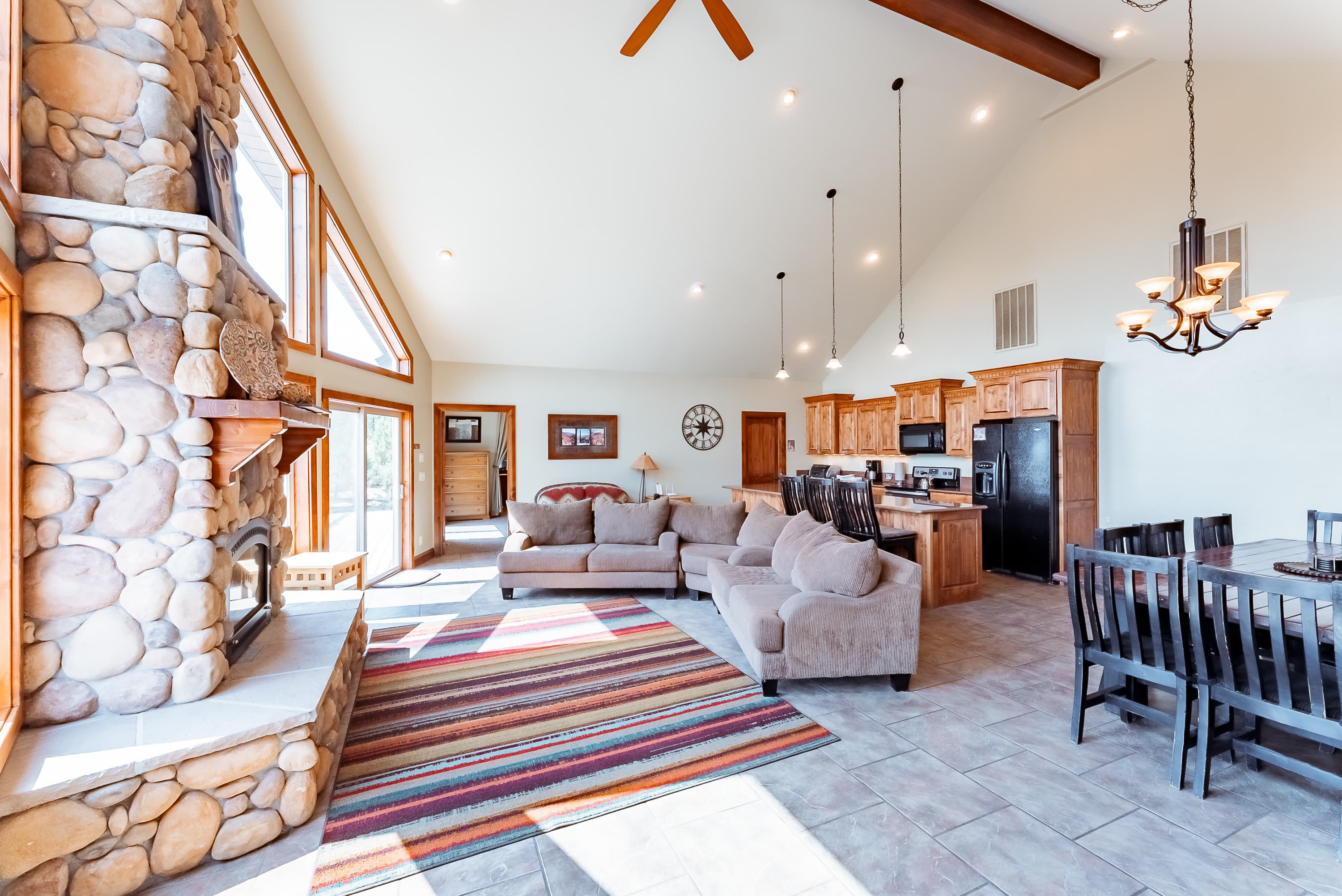 Spacious living area with a stone fireplace, large windows, and modern kitchen.