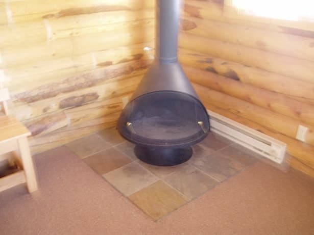 A black metal fireplace sits on a stone hearth in a log cabin interior.