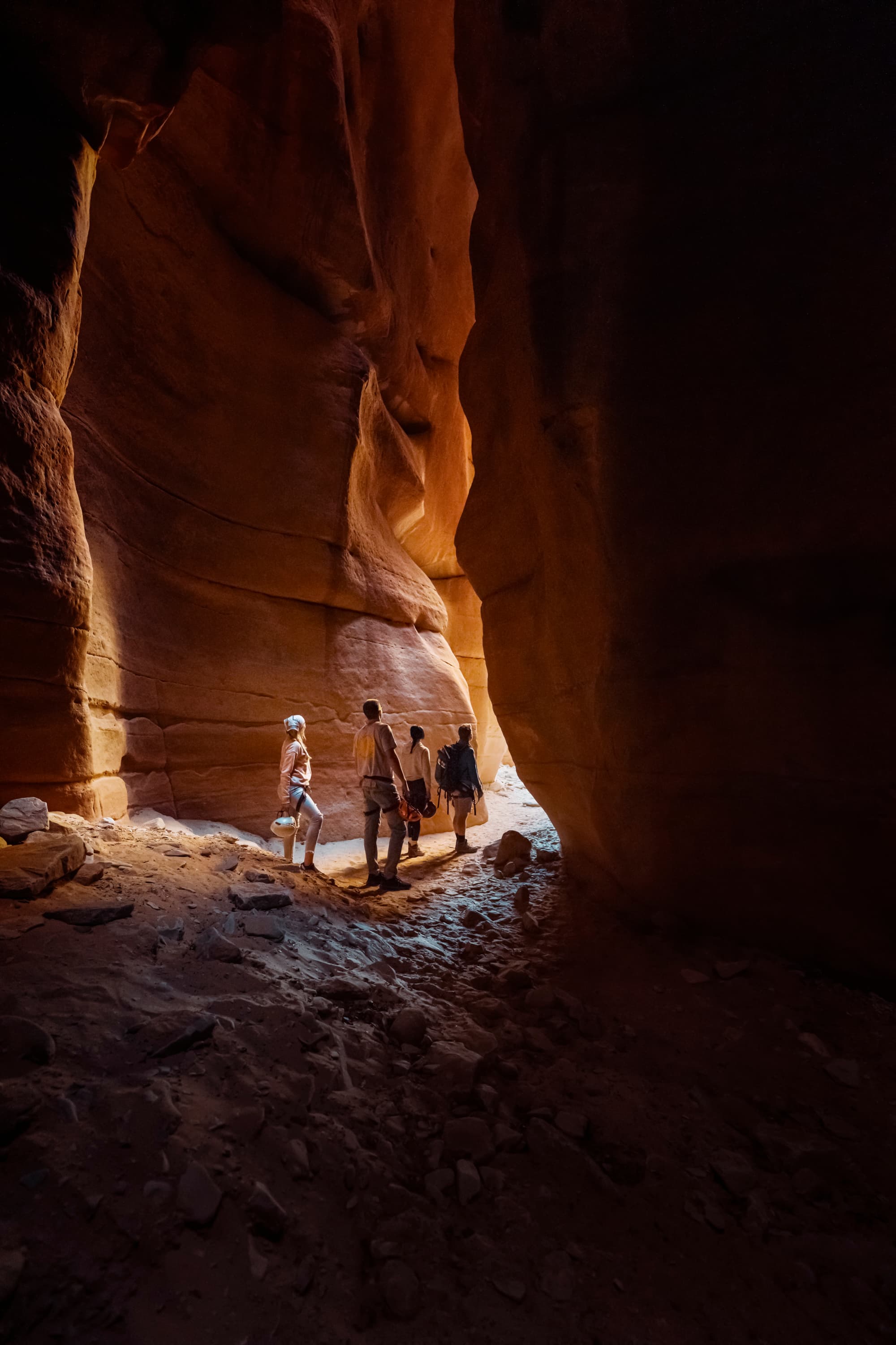 Four hikers explore a narrow canyon illuminated by natural light.