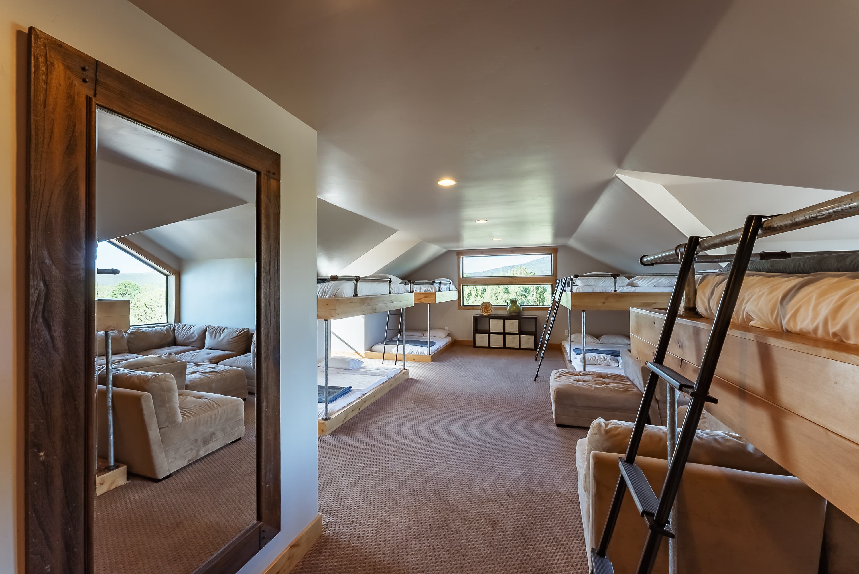 A lofted space featuring a mirror, cozy seating area, and bunk beds with large windows.