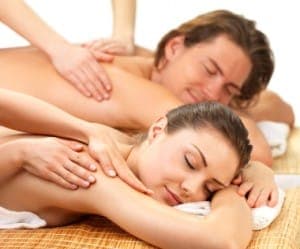 A man and a woman relax during simultaneous massages in a serene setting.