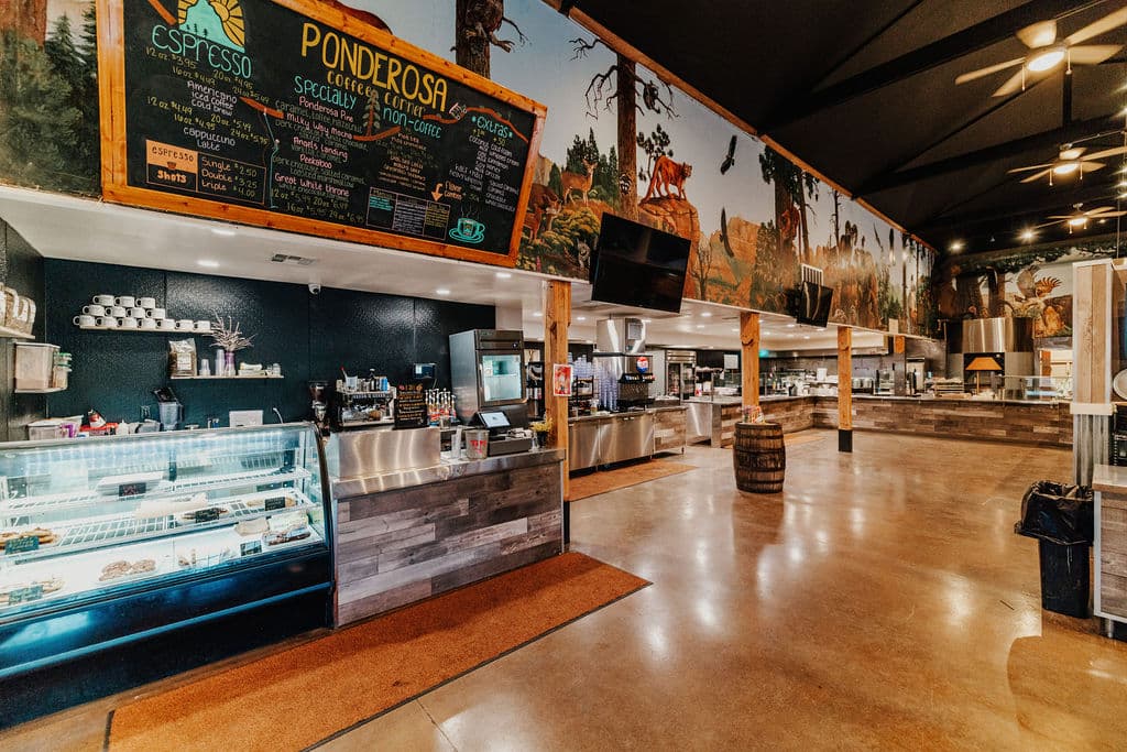 Interior of a cafe featuring a large menu board, counter displays, and rustic decor with a forest mural.