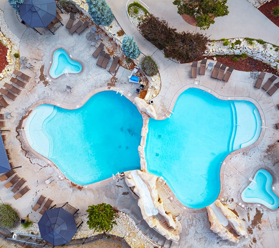 Aerial view of two interconnected swimming pools surrounded by lounge chairs and landscaping.
